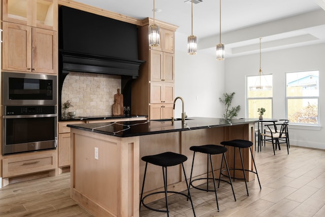 kitchen with appliances with stainless steel finishes, sink, pendant lighting, decorative backsplash, and a kitchen island with sink