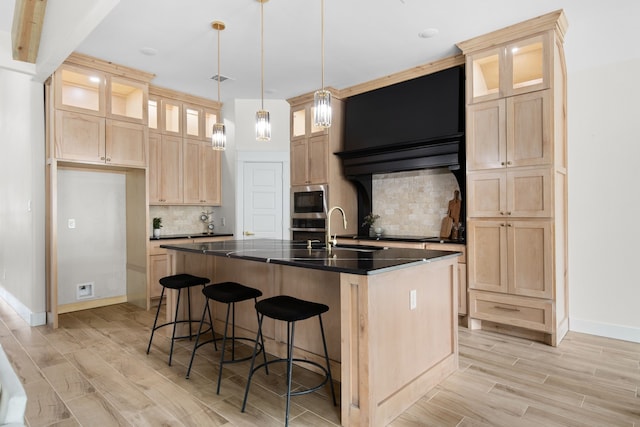 kitchen featuring tasteful backsplash, light hardwood / wood-style flooring, decorative light fixtures, an island with sink, and appliances with stainless steel finishes