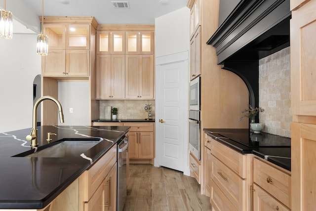 kitchen featuring tasteful backsplash, oven, hanging light fixtures, a center island with sink, and light hardwood / wood-style floors