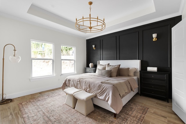 bedroom featuring a tray ceiling, ornamental molding, light hardwood / wood-style flooring, and a chandelier