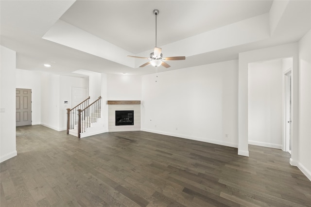 unfurnished living room with dark hardwood / wood-style flooring, a tiled fireplace, a tray ceiling, and ceiling fan