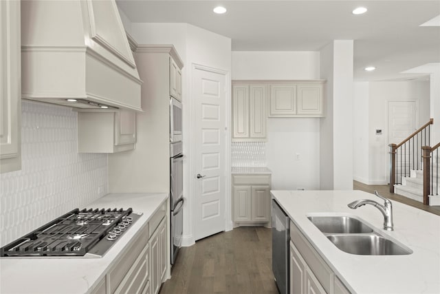 kitchen with stainless steel appliances, premium range hood, sink, and light stone counters