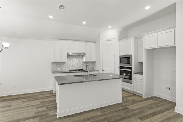 kitchen with built in microwave, sink, oven, white cabinetry, and an island with sink