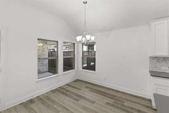 unfurnished dining area featuring hardwood / wood-style floors, a notable chandelier, and vaulted ceiling