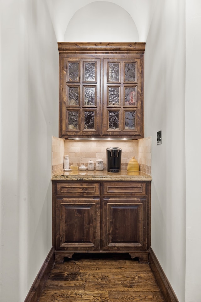 bar with backsplash, dark brown cabinetry, light stone countertops, and dark hardwood / wood-style floors