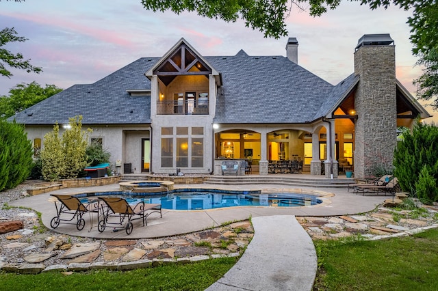 back house at dusk with a patio, a swimming pool with hot tub, and a balcony