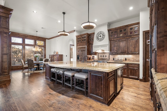 kitchen with dark brown cabinets, an island with sink, hanging light fixtures, decorative backsplash, and light wood-type flooring