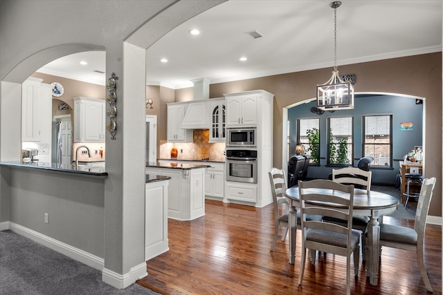 kitchen with white cabinets, crown molding, appliances with stainless steel finishes, a chandelier, and dark hardwood / wood-style floors