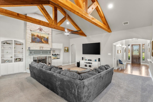 carpeted living room featuring arched walkways, beam ceiling, a fireplace, and visible vents