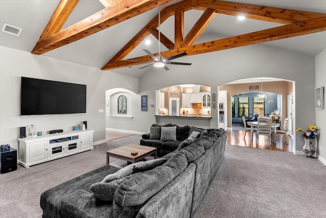 carpeted living room with ceiling fan with notable chandelier, beamed ceiling, and high vaulted ceiling