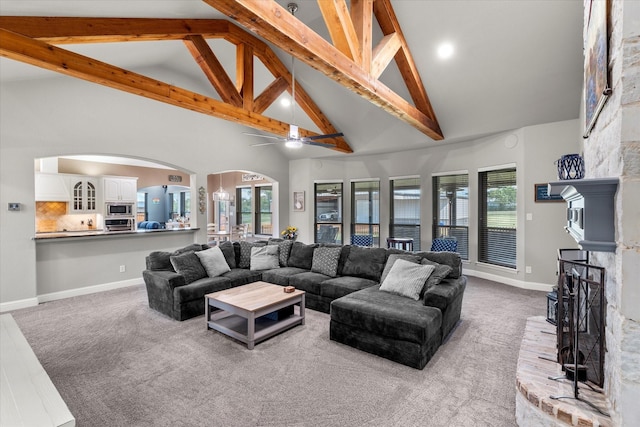 carpeted living room with arched walkways, a brick fireplace, beamed ceiling, and baseboards