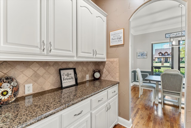 kitchen featuring dark stone countertops, hardwood / wood-style floors, crown molding, decorative backsplash, and white cabinets