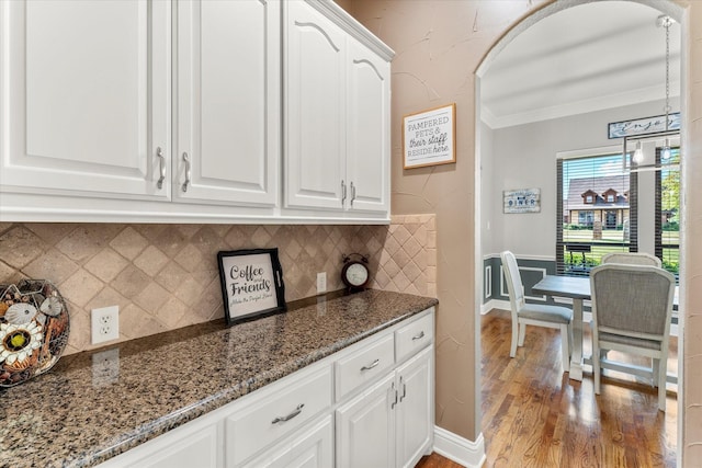 kitchen featuring decorative backsplash, ornamental molding, white cabinetry, dark stone countertops, and wood finished floors