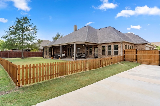 back of house featuring a fenced backyard, brick siding, a yard, a chimney, and a patio area