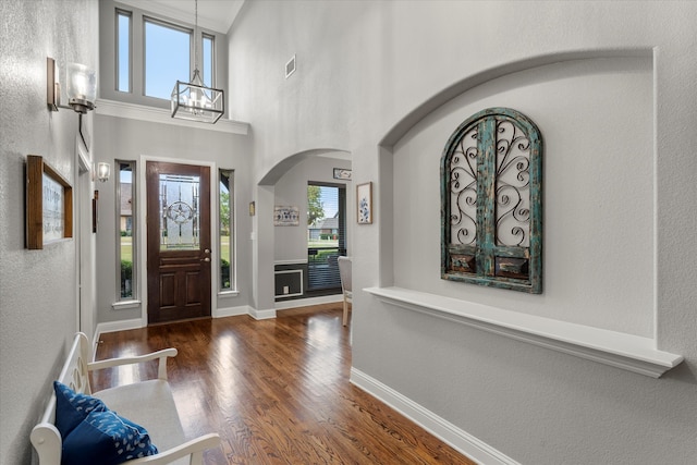 entryway with a healthy amount of sunlight, a towering ceiling, dark hardwood / wood-style flooring, and a notable chandelier