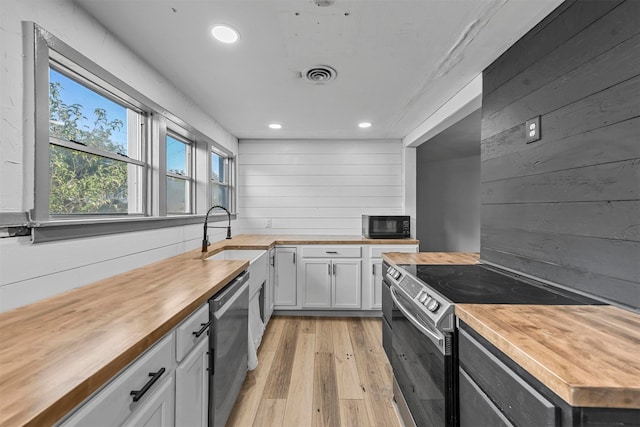 kitchen with light wood-type flooring, sink, white cabinetry, stainless steel appliances, and butcher block countertops