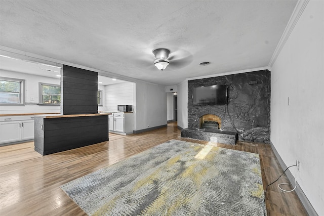 living room with ceiling fan, a textured ceiling, light hardwood / wood-style flooring, a fireplace, and crown molding