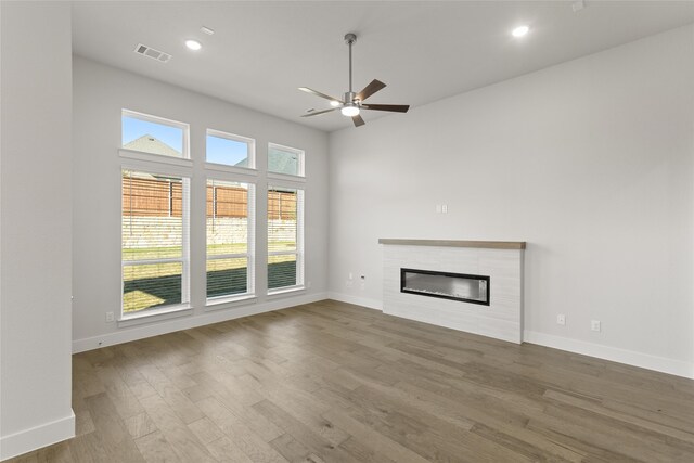 unfurnished living room with ceiling fan, wood-type flooring, and a tile fireplace