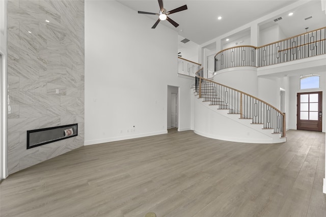 unfurnished living room featuring a high ceiling, ceiling fan, light hardwood / wood-style floors, and a high end fireplace