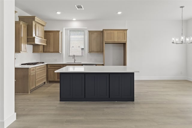 kitchen with stainless steel gas stovetop, hanging light fixtures, light wood-type flooring, sink, and a kitchen island