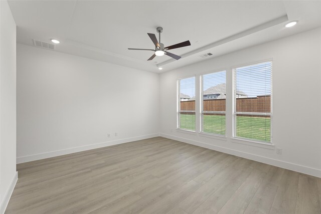 unfurnished room with light wood-type flooring, ceiling fan, and a raised ceiling