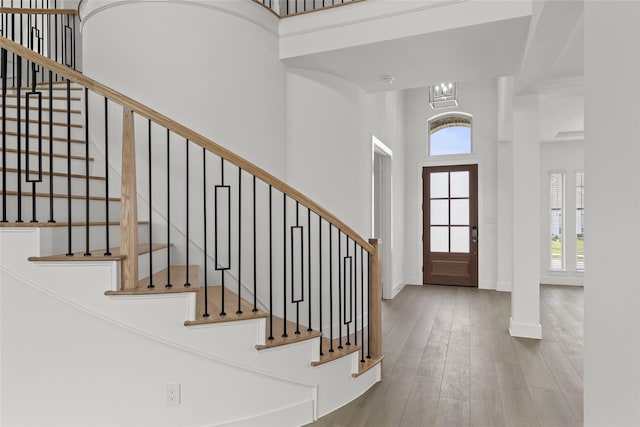 foyer with a high ceiling, wood-type flooring, an inviting chandelier, and a healthy amount of sunlight