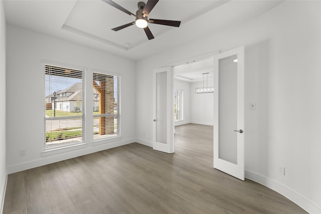 empty room featuring ceiling fan with notable chandelier, a raised ceiling, and wood-type flooring