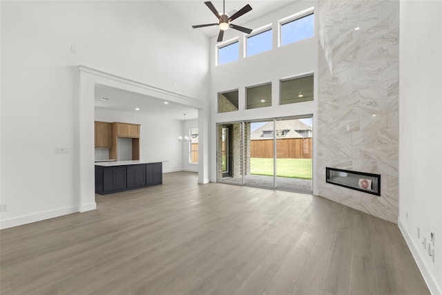 unfurnished living room featuring ceiling fan with notable chandelier, light wood-type flooring, a premium fireplace, and a towering ceiling