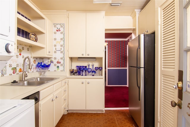 kitchen with white cabinets, stacked washer / drying machine, stainless steel refrigerator, and sink