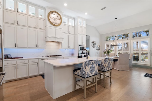 kitchen with white cabinetry, light hardwood / wood-style flooring, lofted ceiling, decorative light fixtures, and a center island with sink