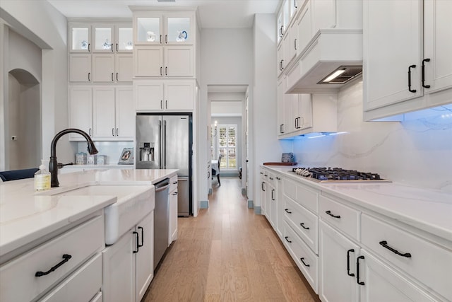 kitchen with white cabinetry, sink, stainless steel appliances, light stone counters, and light hardwood / wood-style floors