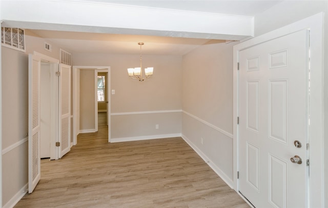 spare room with a notable chandelier and light wood-type flooring