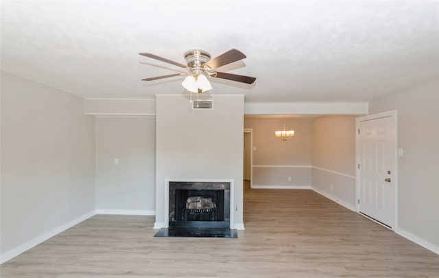 unfurnished living room featuring ceiling fan with notable chandelier, light hardwood / wood-style floors, and a premium fireplace