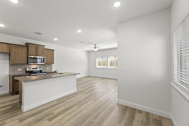 kitchen with dark stone countertops, light hardwood / wood-style flooring, stainless steel appliances, ceiling fan, and decorative backsplash