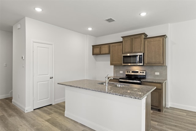 kitchen featuring light hardwood / wood-style flooring, stainless steel appliances, backsplash, and a kitchen island with sink