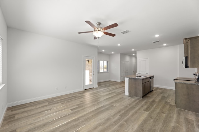 kitchen with light wood-type flooring, sink, an island with sink, and ceiling fan