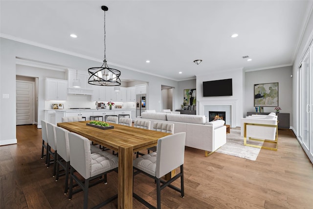 dining space with recessed lighting, light wood-style flooring, crown molding, and a glass covered fireplace