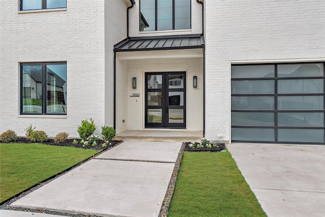 property entrance featuring a garage, a lawn, metal roof, a standing seam roof, and french doors