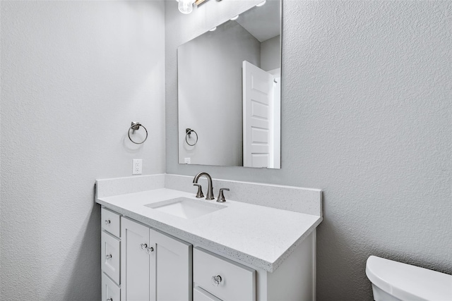 bathroom with a textured wall, vanity, and toilet