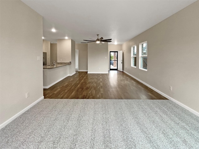 unfurnished living room featuring dark colored carpet, a ceiling fan, and baseboards