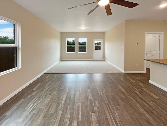 unfurnished living room featuring a wealth of natural light, ceiling fan, baseboards, and wood finished floors