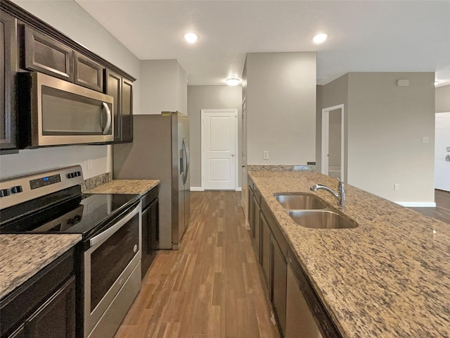 kitchen featuring light stone counters, appliances with stainless steel finishes, dark brown cabinetry, a sink, and wood finished floors