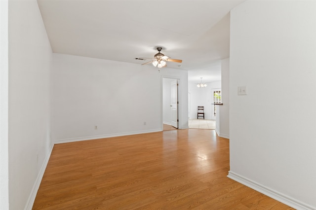 empty room with ceiling fan with notable chandelier and light wood-type flooring