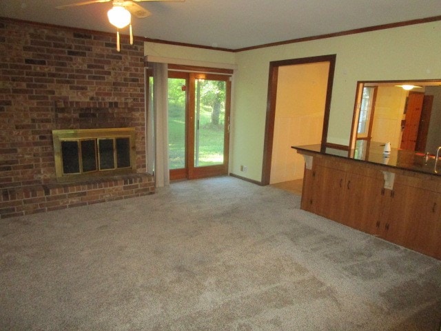 unfurnished living room featuring crown molding, ceiling fan, a brick fireplace, and carpet floors