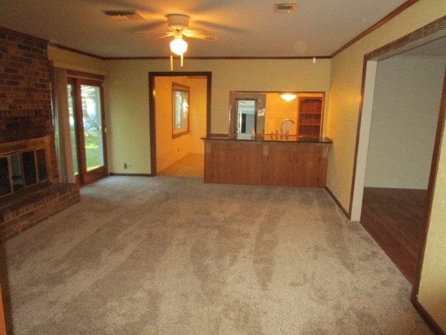 unfurnished living room with crown molding, a brick fireplace, ceiling fan, and carpet floors