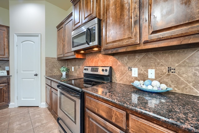 kitchen with dark stone countertops, backsplash, stainless steel appliances, and light tile patterned flooring