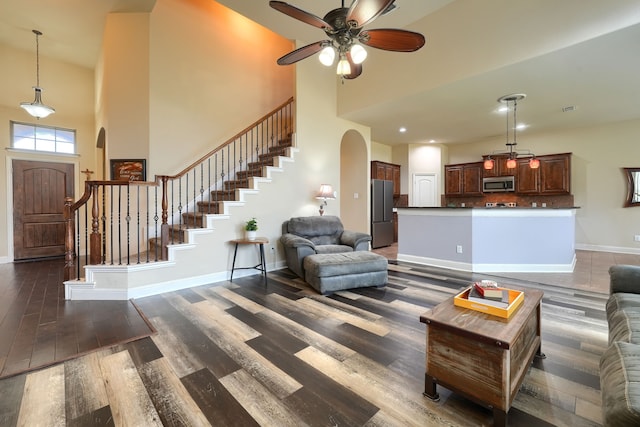 living room with ceiling fan, a towering ceiling, and dark hardwood / wood-style flooring