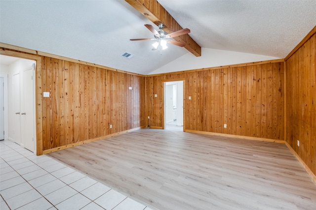 spare room featuring a textured ceiling, ceiling fan, light wood-type flooring, and wooden walls