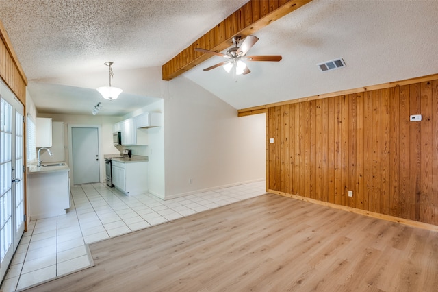 unfurnished living room with ceiling fan, wooden walls, light hardwood / wood-style floors, and lofted ceiling with beams