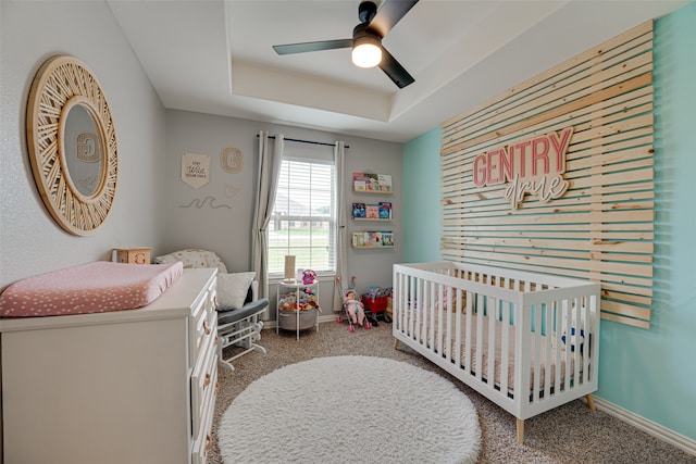 bedroom featuring a tray ceiling, ceiling fan, carpet, and a crib